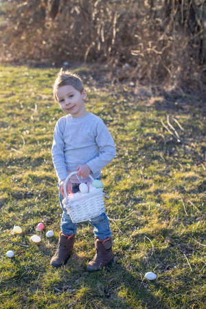 Cute toddler boy, gathering easter colorful eggs in a basket in the park, springtime
