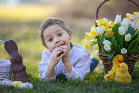 Beautiful stylish toddler child, boy, playing with Easter decoration in the park, springtimeの写真素材
