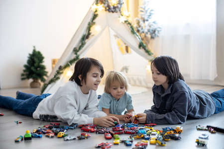 Cute toddler child and his older brothers, playing with colofrul cars, different sizes and colors on...