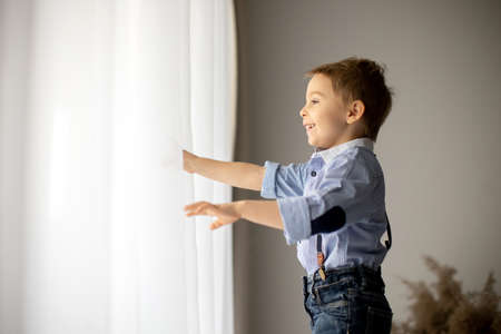 Beautiful fashion preschool child, boy, having fun at home in bed, looking out of the window, springtimeの写真素材