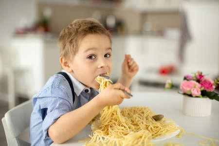 Cute preschool child, blond boy, eating spaghetti at home, making a mess everywhere, funny momentsの写真素材