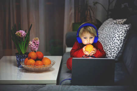 Child, holding orange, watching movie on a computer night time at home