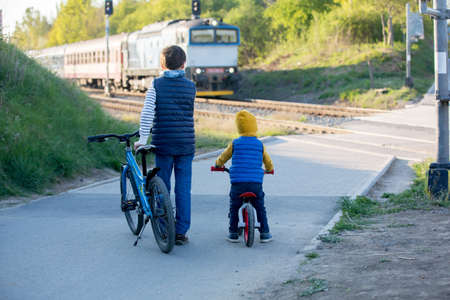 Children, boy brothers, waiting on a railroad cross to pass a train, springtimeの写真素材