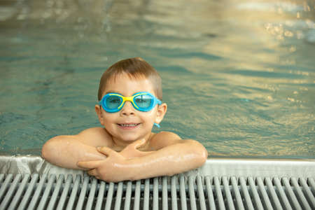 Child, taking swimming lessons in a group of children in indoor pool, enjoying learning