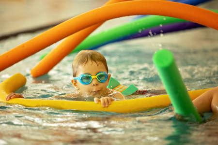 Child, taking swimming lessons in a group of children in indoor pool, enjoying learningの写真素材