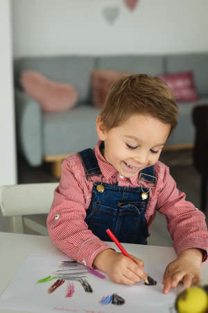 Cute boy, child in red shirt, drawing picture for Mothers day, little chicks on the table playing