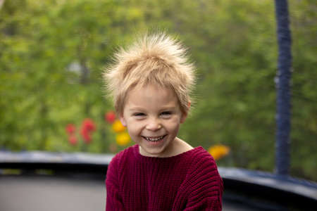 Cute little boy with static electric hair, having his funny portrait taken outdoors on a trampolineの写真素材