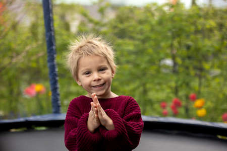 Cute little boy with static electric hair, having his funny portrait taken outdoors on a trampolineの写真素材