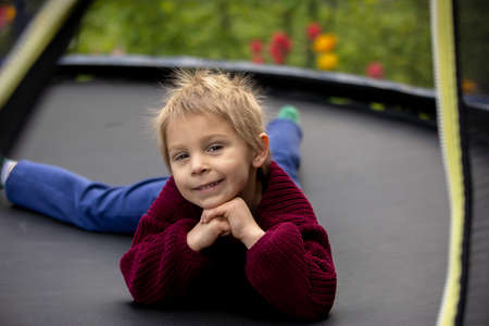 Cute little boy with static electric hair, having his funny portrait taken outdoors on a trampolineの写真素材