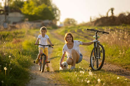 Cute child with pet dog, riding a bike in a rural field on sunset, springtime