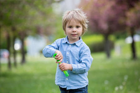 Blond toddler child, cute boy in casual clothing, playing with soap bubbles in the park, running happilyの写真素材
