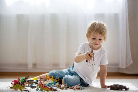 Blond child, toddler boy, playing with plastic animal toys at home, soft back lightの写真素材