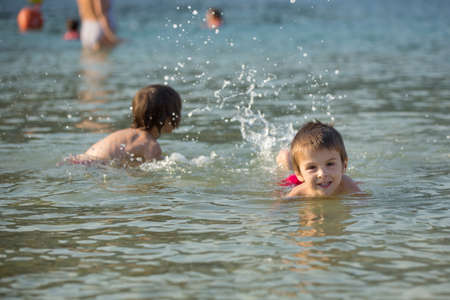 Two sweet children, boy brothers, splashing each other with water on the beach on sunsetの写真素材