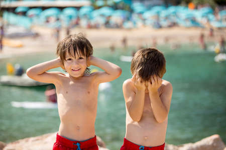 Two children on the beach, boys, playing and making funny faces, do not hear, do not see, enjoying their holidayの写真素材