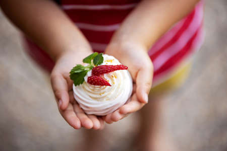 Cute child, boy, eating small cupcake of Pavlova desert, light egg and sugar desert with cream and strawberries, enjoyingの写真素材