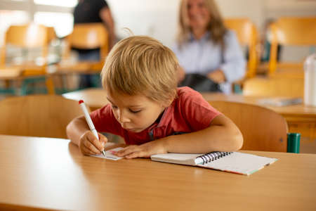 Preschool child, sitting on a desk at school, having lesson, learning new things