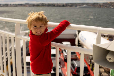 Children, experience ride on a ferry on a fjord, strong wind on the deck of a ferry on a sunny dayの写真素材