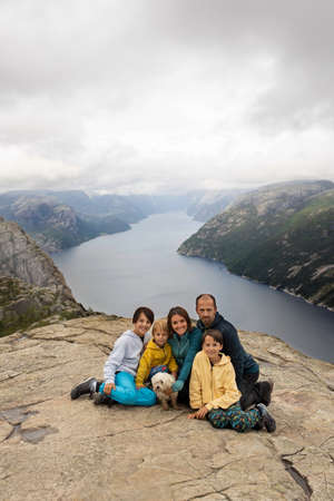 Family, enjoying the hike to Preikestolen, the Pulpit Rock in Lysebotn, Norway on a rainy day, toddler climbing with his pet dog the one of the most scenic fjords in Norwayの写真素材