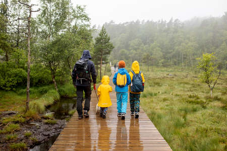 Family, enjoying the hike to Preikestolen, the Pulpit Rock in Lysebotn, Norway on a rainy day, toddler climbing with his pet dog the one of the most scenic fjords in Norwayの写真素材