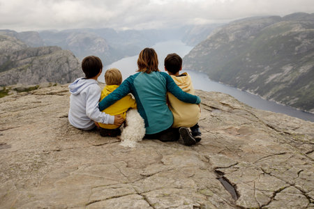 Family, enjoying the hike to Preikestolen, the Pulpit Rock in Lysebotn, Norway on a rainy day, toddler climbing with his pet dog the one of the most scenic fjords in Norwayの写真素材