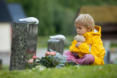 Sad little child, blond boy, standing in the rain on cemetery, sad person, mourningの写真素材