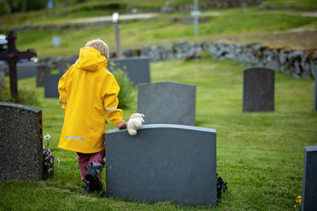 Sad little child, blond boy, standing in the rain on cemetery, sad person, mourningの写真素材