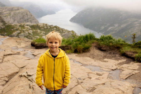 Family, enjoying the hike to Preikestolen, the Pulpit Rock in Lysebotn, Norway on a rainy day, toddler climbing with his pet dog the one of the most scenic fjords in Norwayの写真素材