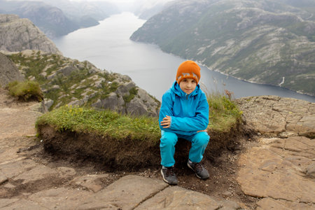 Family, enjoying the hike to Preikestolen, the Pulpit Rock in Lysebotn, Norway on a rainy day, toddler climbing with his pet dog the one of the most scenic fjords in Norwayの写真素材