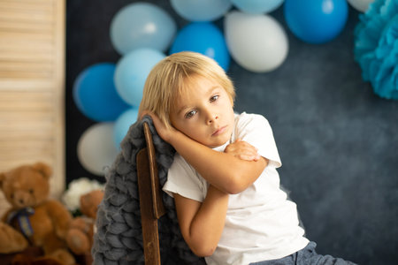 Cute blond toddler preschool boy, reading a book and opening present on Christmas on cozy home, lights and decorationの写真素材