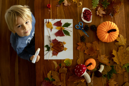 Child, applying leaves using glue, scissors, and paint, while doing arts and crafts at home or at schoolの写真素材