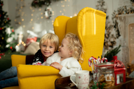 Cute little toddler curly girl in winter christmas sweater, sitting in cozy room, decorated for christmasの写真素材