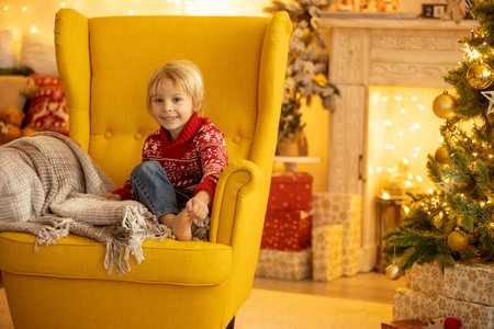 Cute child, boy, sitting on a yellow armchair in a decorated room for Christmas, cozy placeの写真素材
