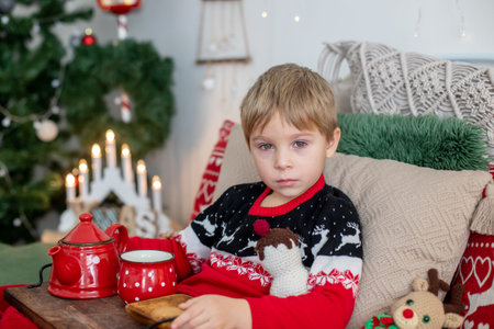 Small toddler child, lying sick in bed, red eyes, drinking tea on christmas at home