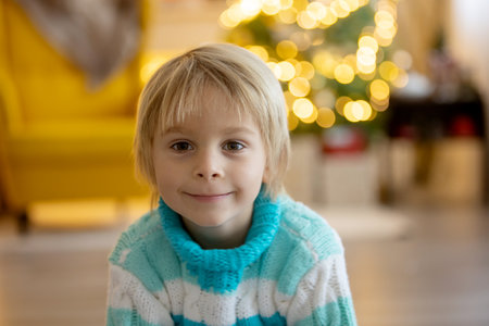 Cute child, boy, sitting on a yellow armchair in a decorated room for Christmas, cozy place