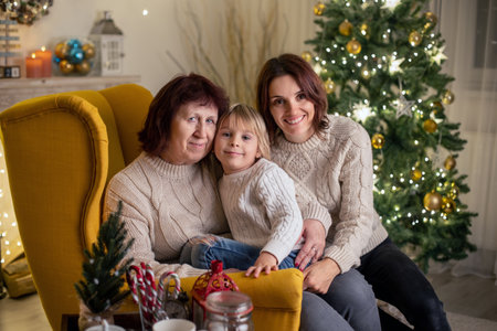Cute child, boy, sitting in yellow armchair in a decorated room for Christmas with mother and grandmotherの写真素材