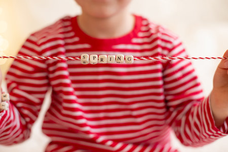 Cute preschool boy, playing with white and red bracelets. Martenitsa, white and red strains of yarn, Bulgarian folklore tradition, welcoming spring in March, adornment symbol, wish for good heathの写真素材
