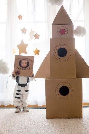 Sweet toddler boy, dressed as an astronaut, playing at home with cardboard rocket and handmade helmet from boxの写真素材