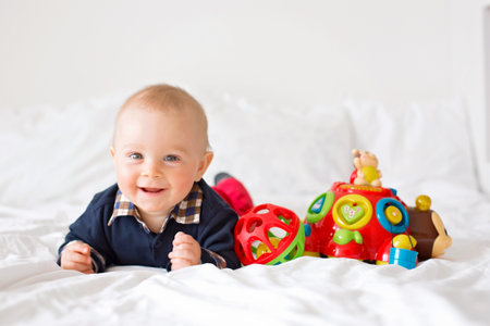Sweet toddler boy, playing with colorful toys in bed, daytime. Childhood happiness concept, early development toysの写真素材