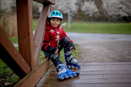 Little child, preschool boy in protective equipment and rollers blades, riding on walkway in parkの写真素材