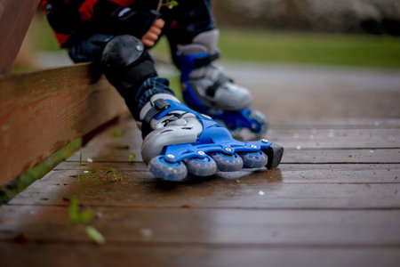Little child, preschool boy in protective equipment and rollers blades, riding on walkway in parkの写真素材
