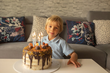 Beautiful adorable five year old boy in blue shirt, celebrating his birthday with homemade cakeの写真素材