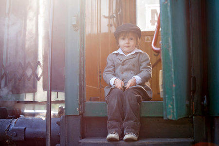 Two boys, dressed in vintage clothing and hat, with suitcase, on a railway stationの写真素材