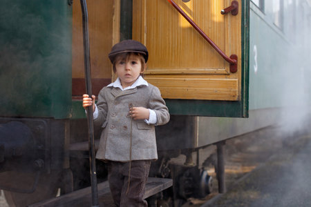 Two boys, dressed in vintage clothing and hat, with suitcase, on a railway stationの写真素材