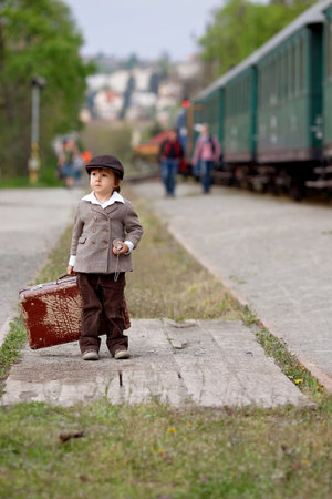 Two boys, dressed in vintage clothing and hat, with suitcase, on a railway stationの写真素材