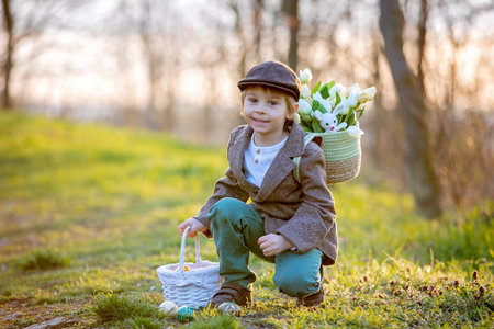 Beautiful stylish toddler child, boy, playing with Easter decoration in the park, springtime on sunsetの写真素材
