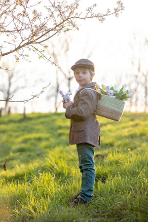 Beautiful stylish toddler child, boy, playing with Easter decoration in the park, springtime on sunsetの写真素材
