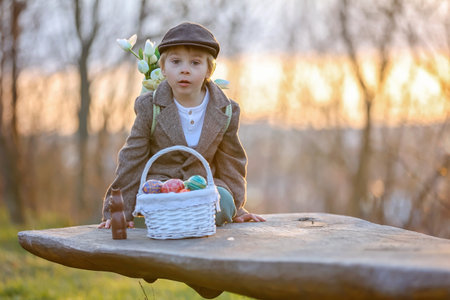 Beautiful stylish toddler child, boy, playing with Easter decoration in the park, springtime on...