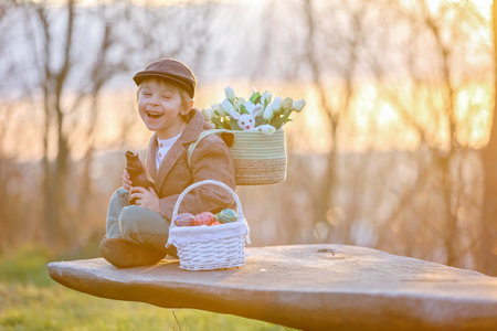 Beautiful stylish toddler child, boy, playing with Easter decoration in the park, springtime on...