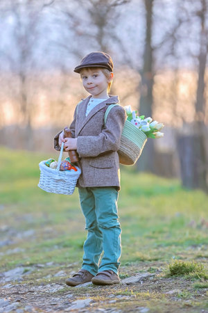 Beautiful stylish toddler child, boy, playing with Easter decoration in the park, springtime on sunsetの写真素材