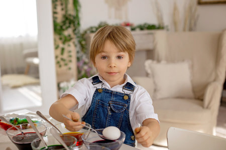 Happy childen, siblings, coloring eggs with colorful waters for Easter at home, sunny room